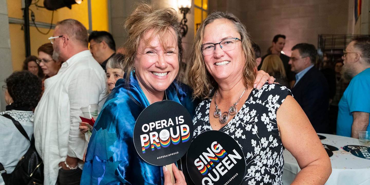 Two women smiling with Opera is Proud signs_PC_Drew Altizer Photography.