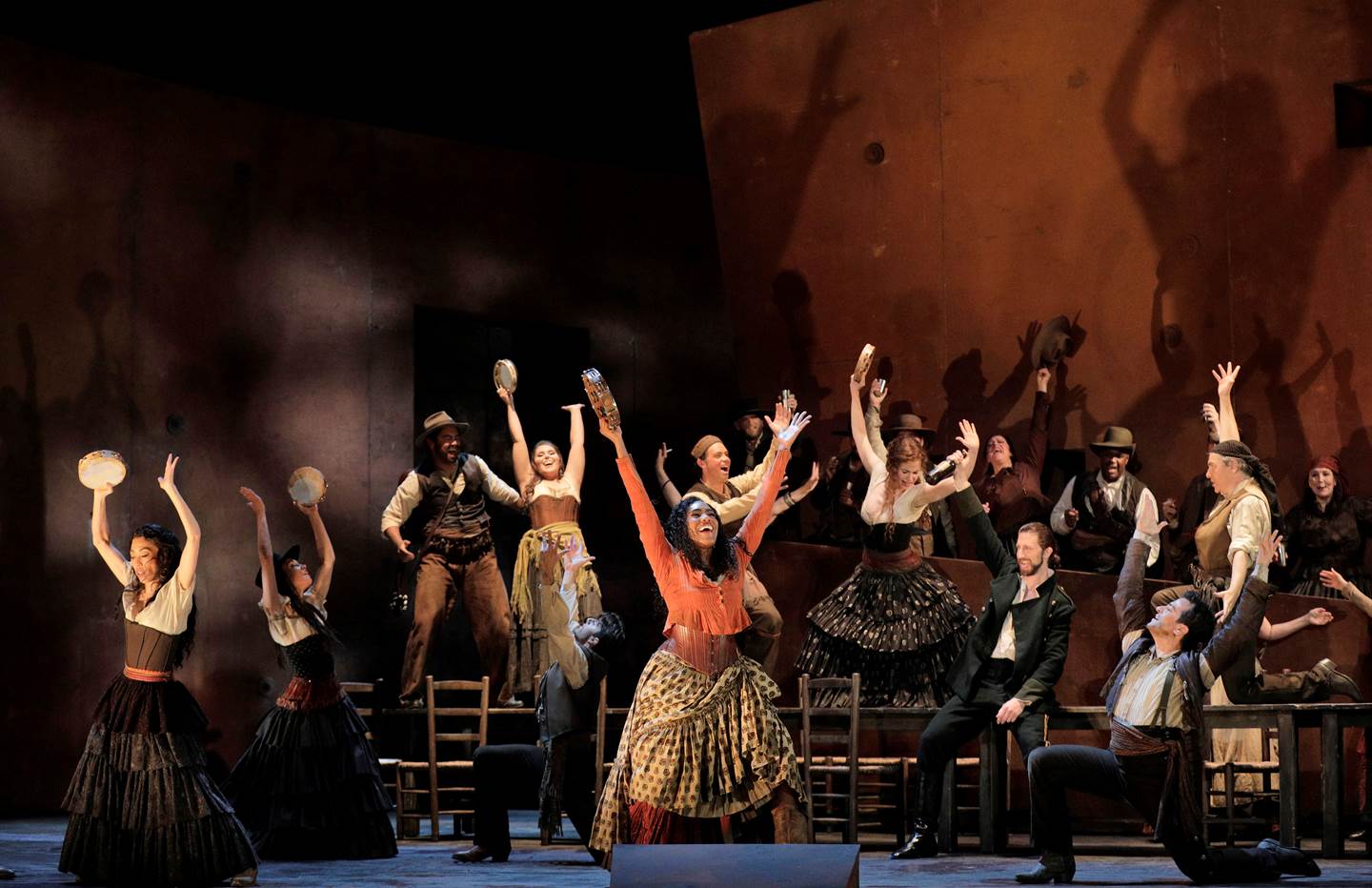 Cast of Carmen with their hands in the air, standing on chairs and tables