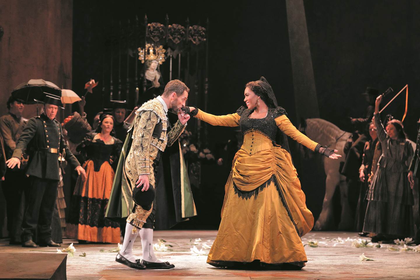 A man in a troubadour outfit kissing the hand of a woman in an elegant yellow dress in the opera Carmen