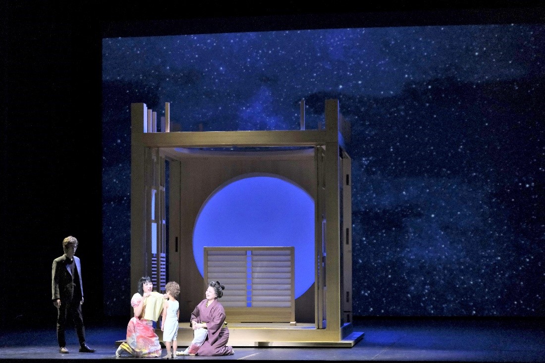 A woman handling child on stage along with older woman and man in the background