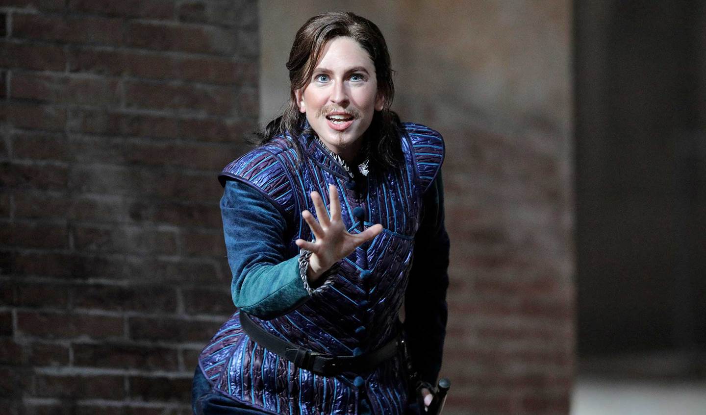 Romeo and Juliet's Stephano in a blue outfit looking at camera with their hand out in front of them.