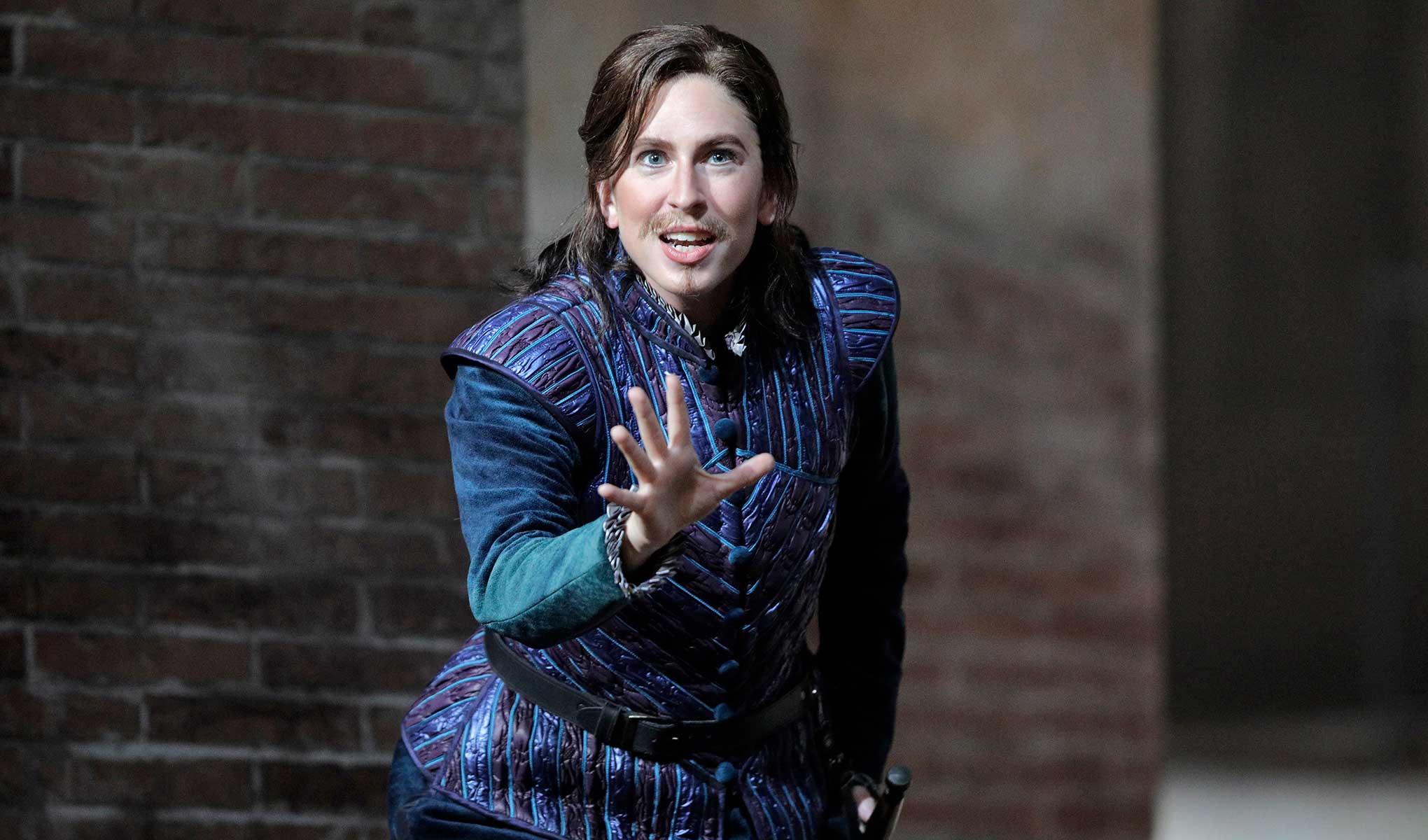 Romeo and Juliet's Stephano in a blue outfit looking at camera with their hand out in front of them.