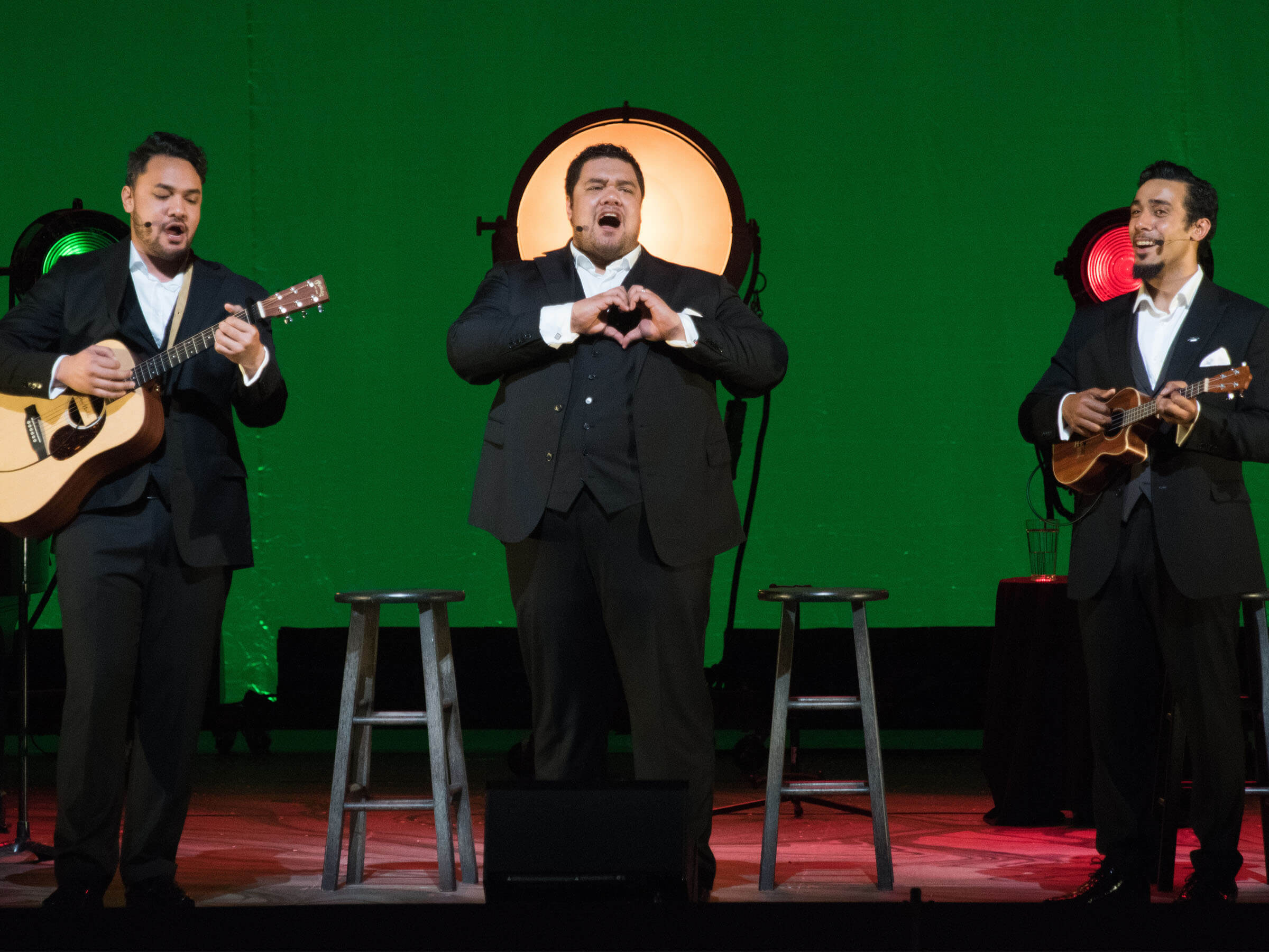 Michael Bragg singing on stage with a guitar player and ukulele player