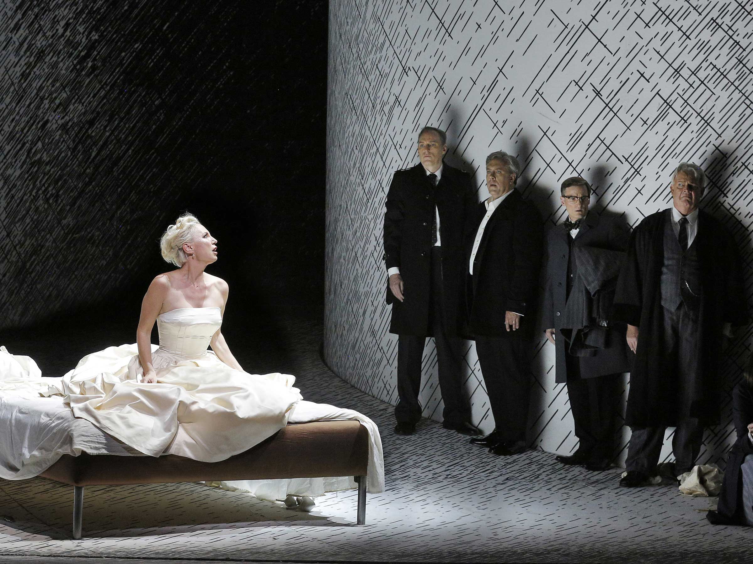woman in white gown sitting on bench with men in suits standing up against a wall.