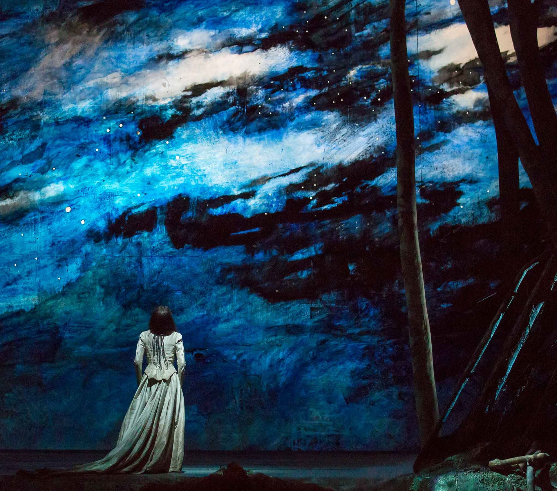A scene from Rusalka depicted as a painted image with a woman looking at the sky while in the woods.