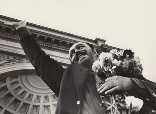 black and white photo of Luciano Pavarotti from 1979 park concert holding a bouquet of flowers and waiving