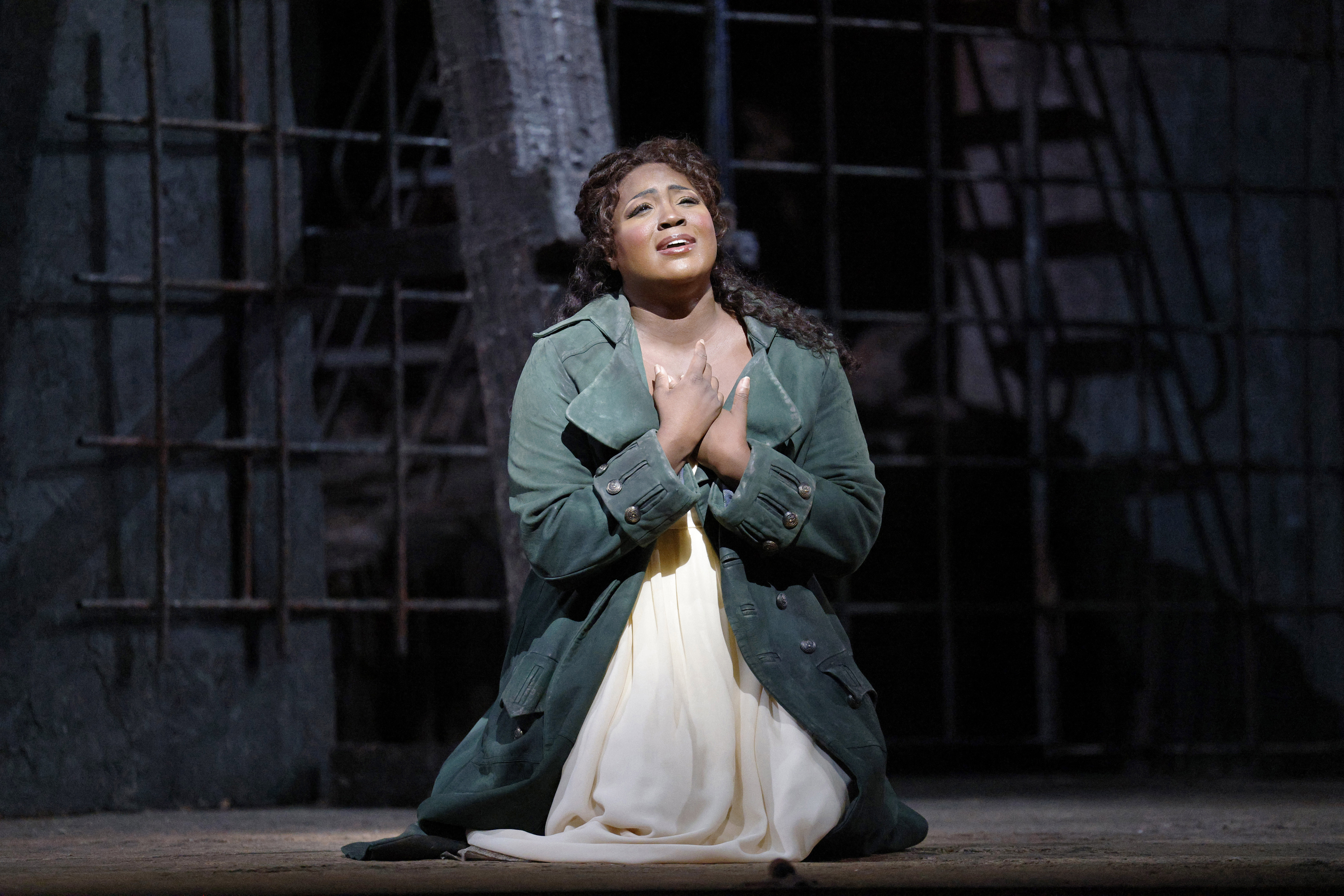 Women nealed on stage crossing hands singing with spotlight on her