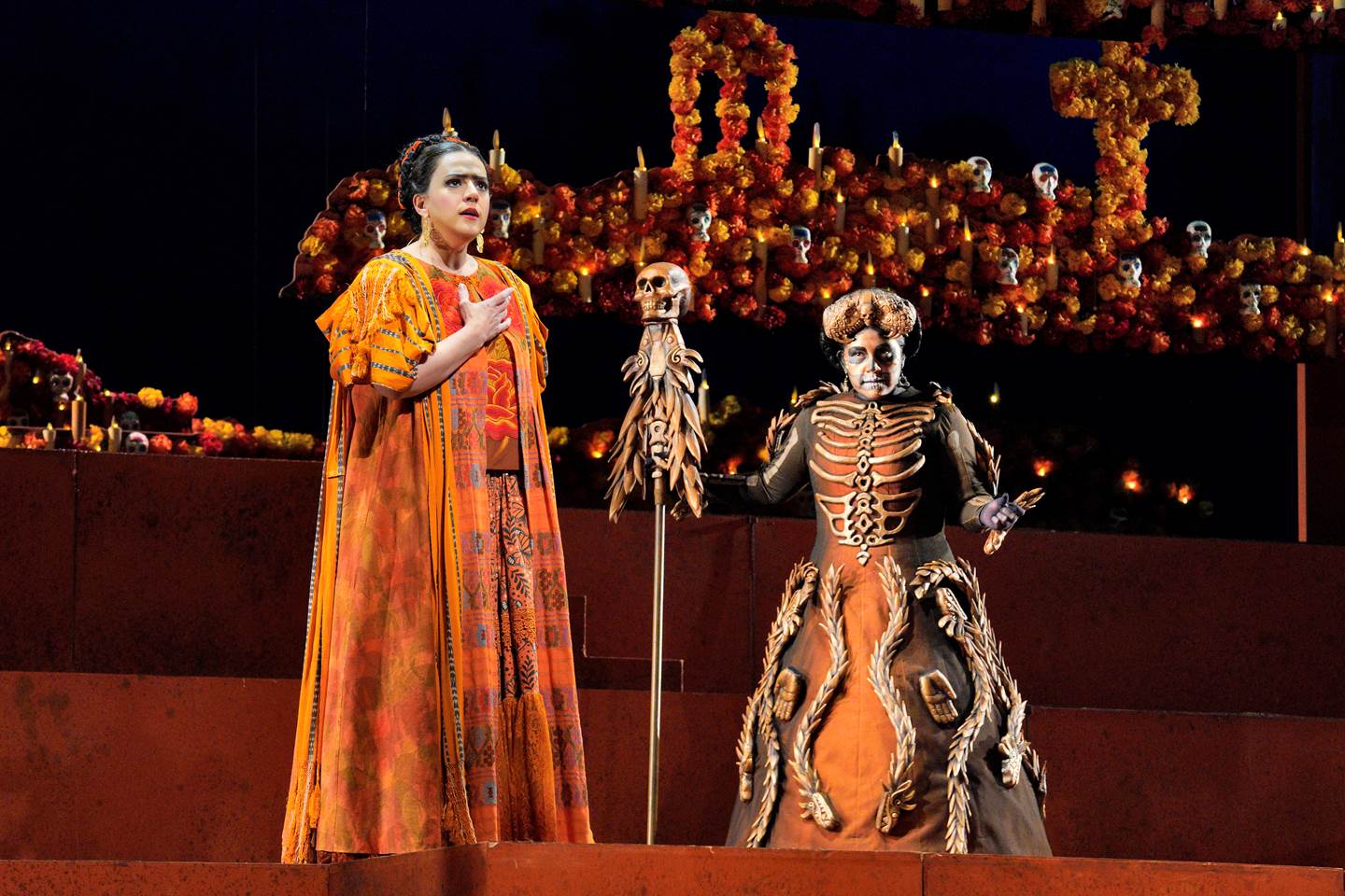 Scene from Frida Two women in costumes standing on a stage in front of skeletons.
