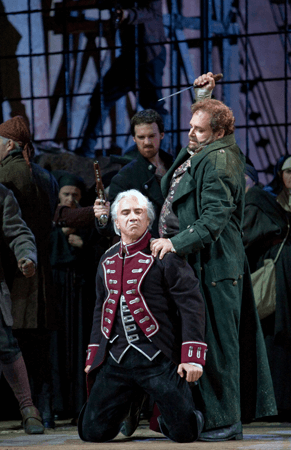 Opera character on his knees with another behind him getting ready to stab him with a knife