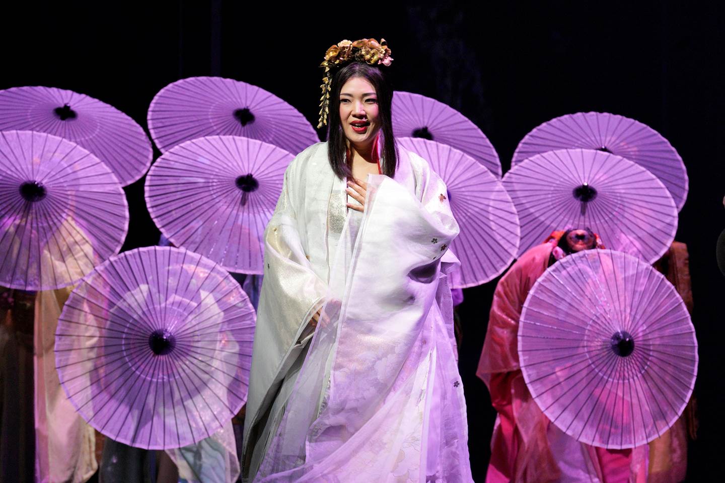 Madame Butterfly with cast behind her hiding behind purple parasols