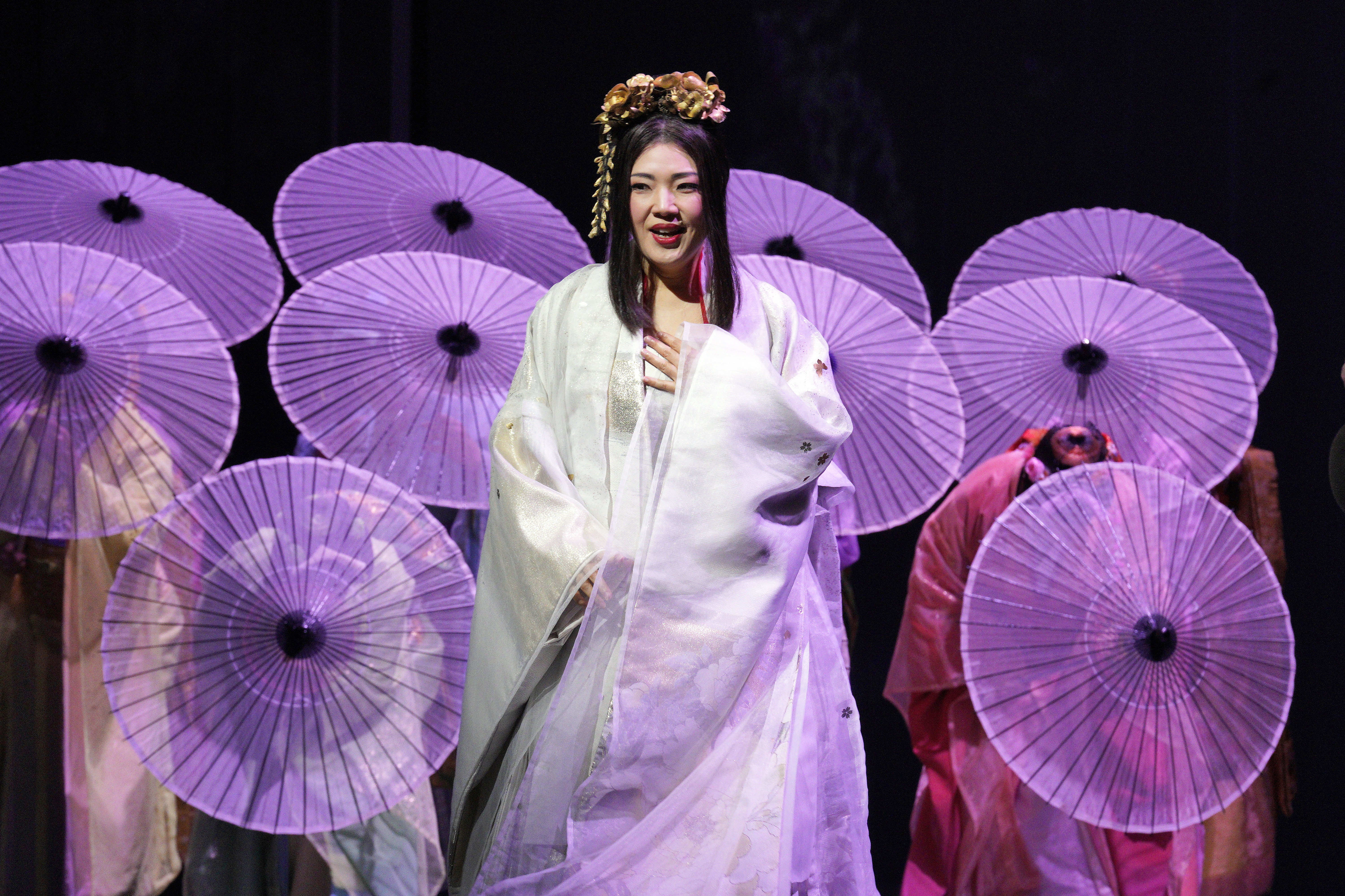 Madame Butterfly with cast behind her hiding behind purple parasols