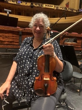 Kay Stern sitting on a chair holding here violin