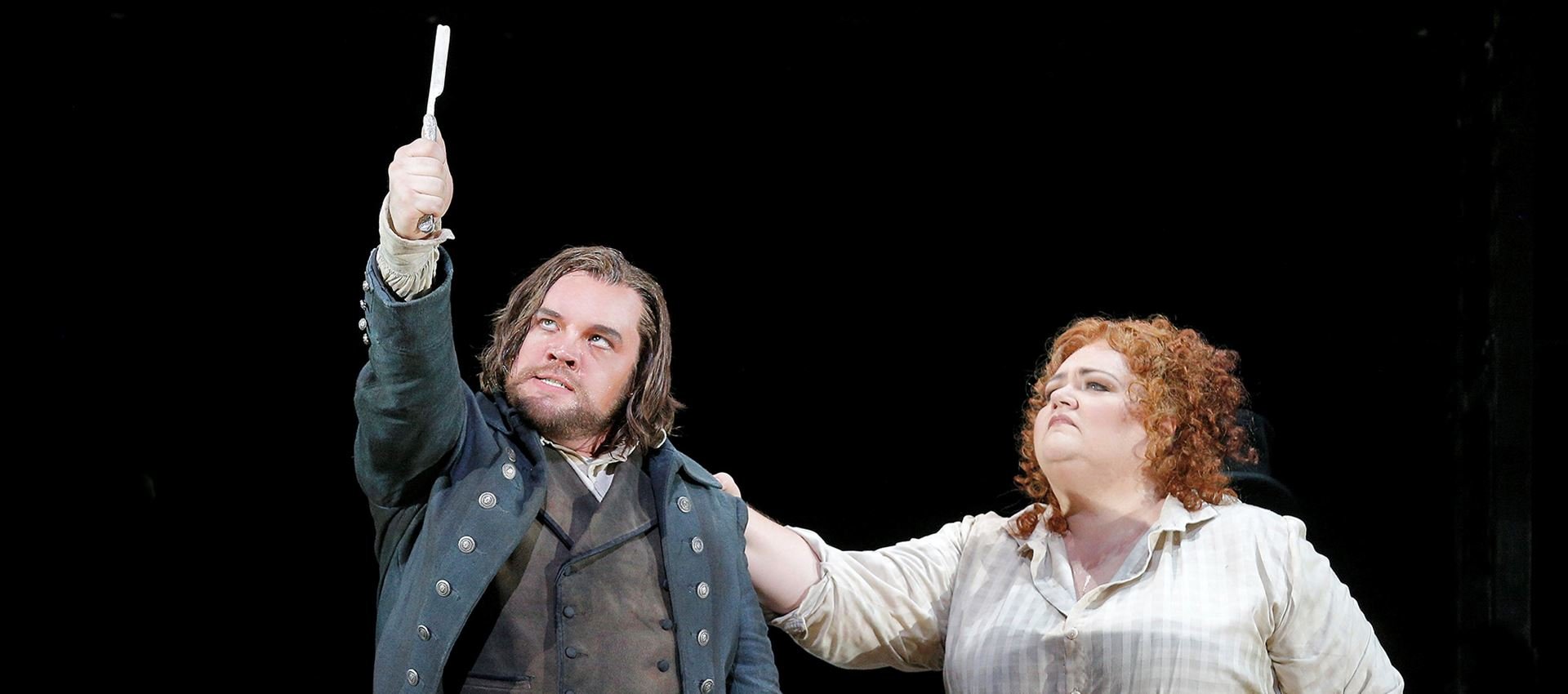 Sweeney Todd is holding up a knife while a woman has her hand on his shoulder
