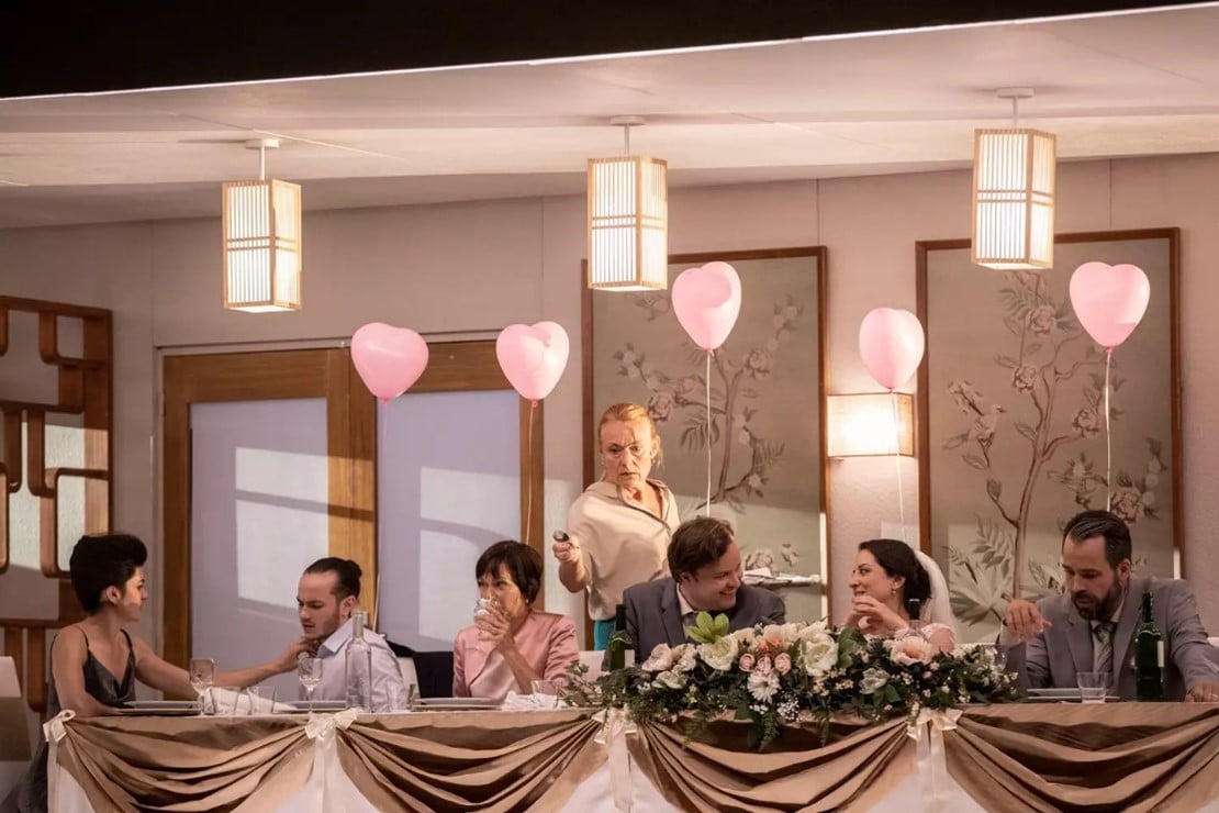 A bride and groom sitting at the wedding party table with pink heart balloons tied to the back of each chair.