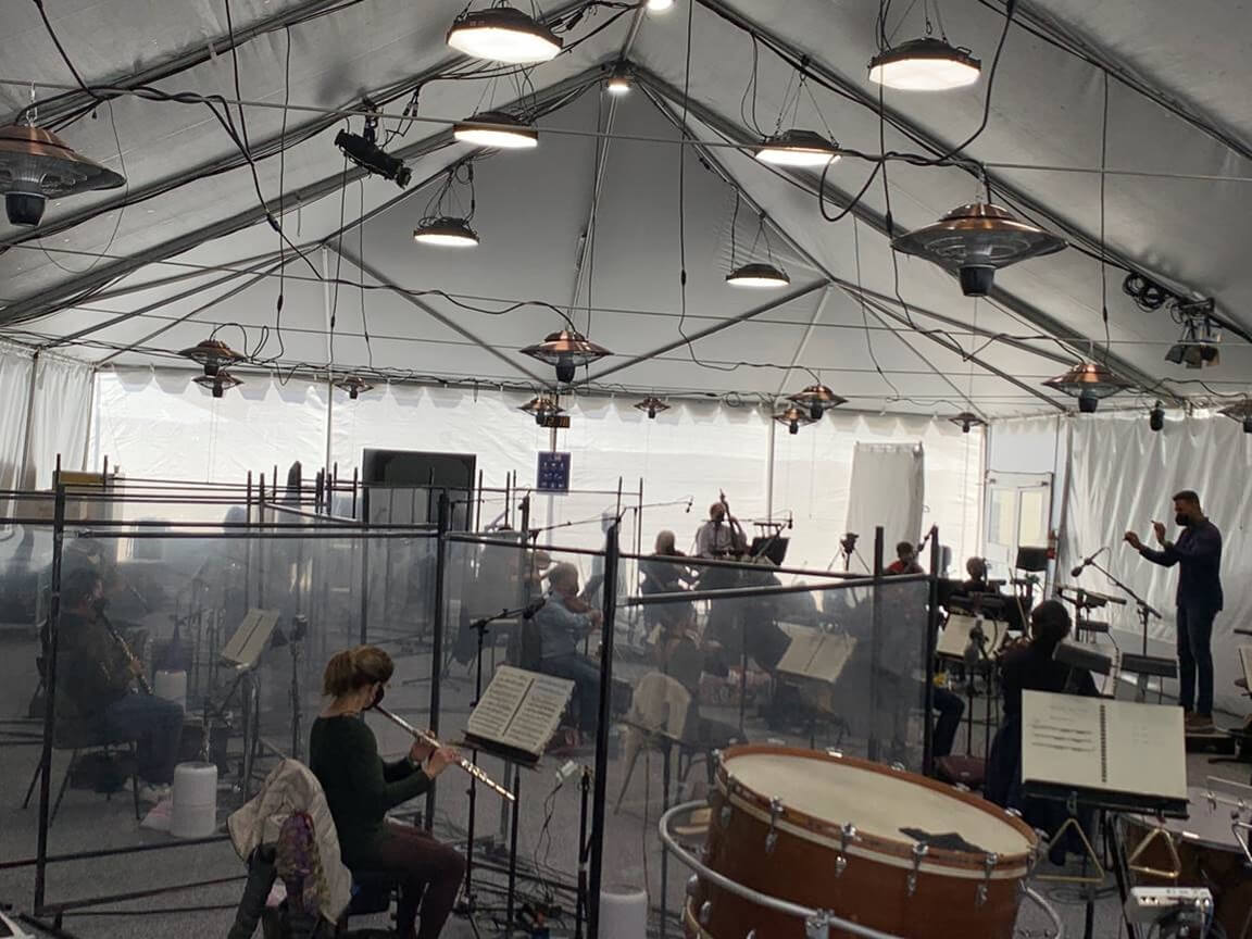 Opera orchestra rehearsals in a tent and everyone separated by glass partitions