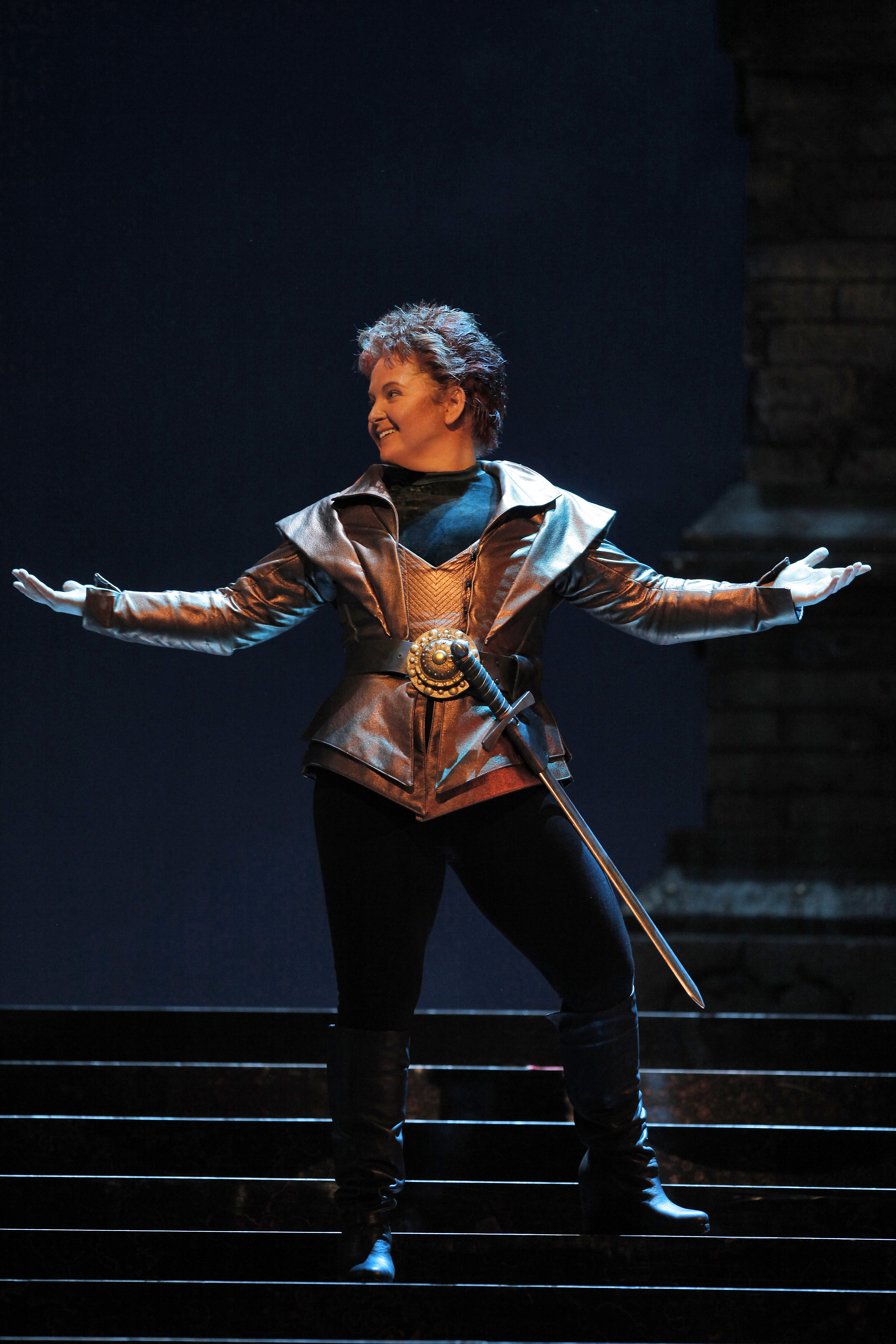 a women standing on stairs (on a stage) with her arms spread a part