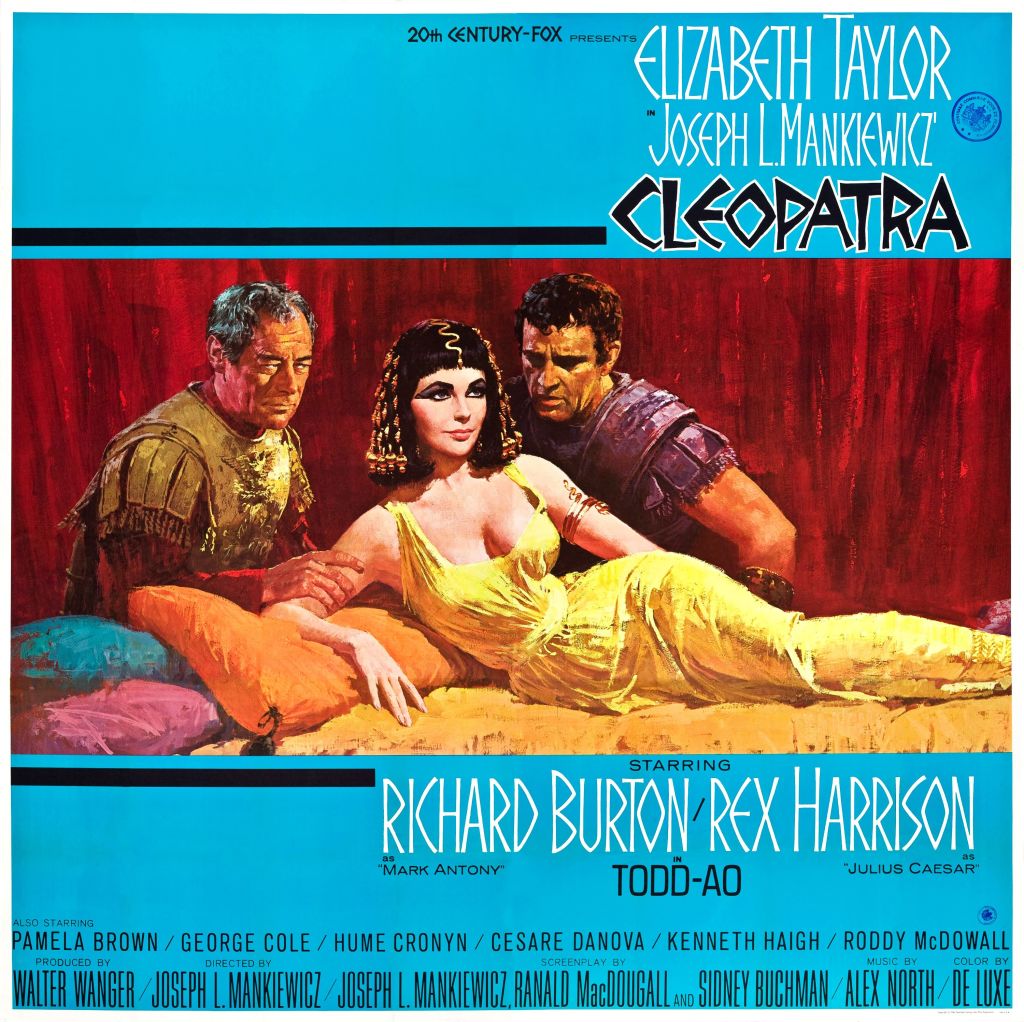 Elizabeth Taylor as Cleopatra poses laying down with two men staring at her
