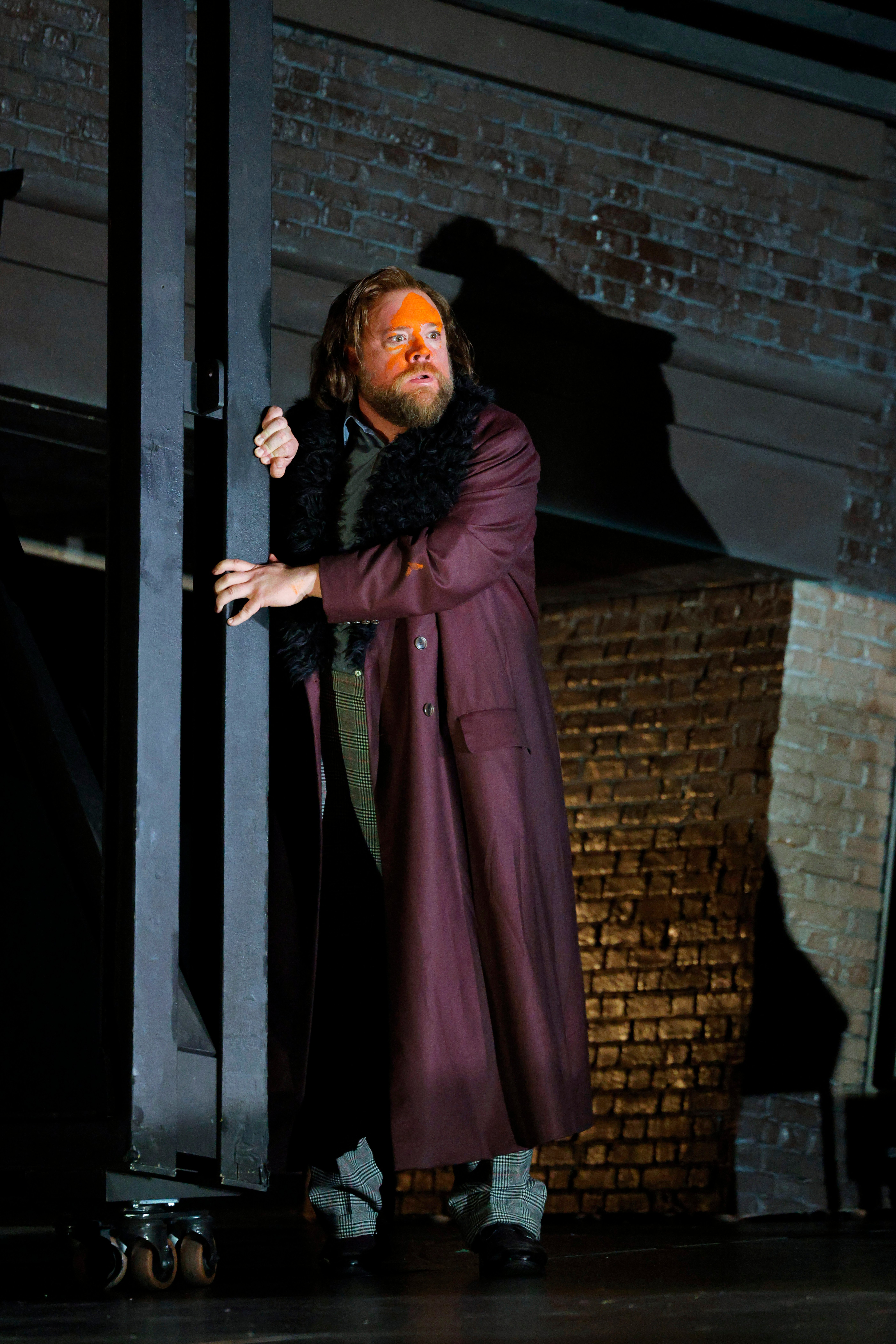 man with purple coat holding on to building