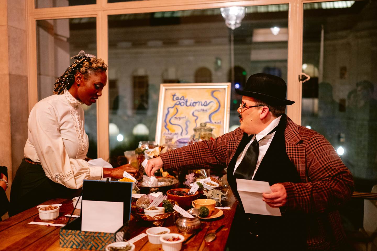 Scene from San Francisco Opera&#39;s Elixir Encounter featuring a man in a hat and plaid jacket purchasing tea potions from a merchant.