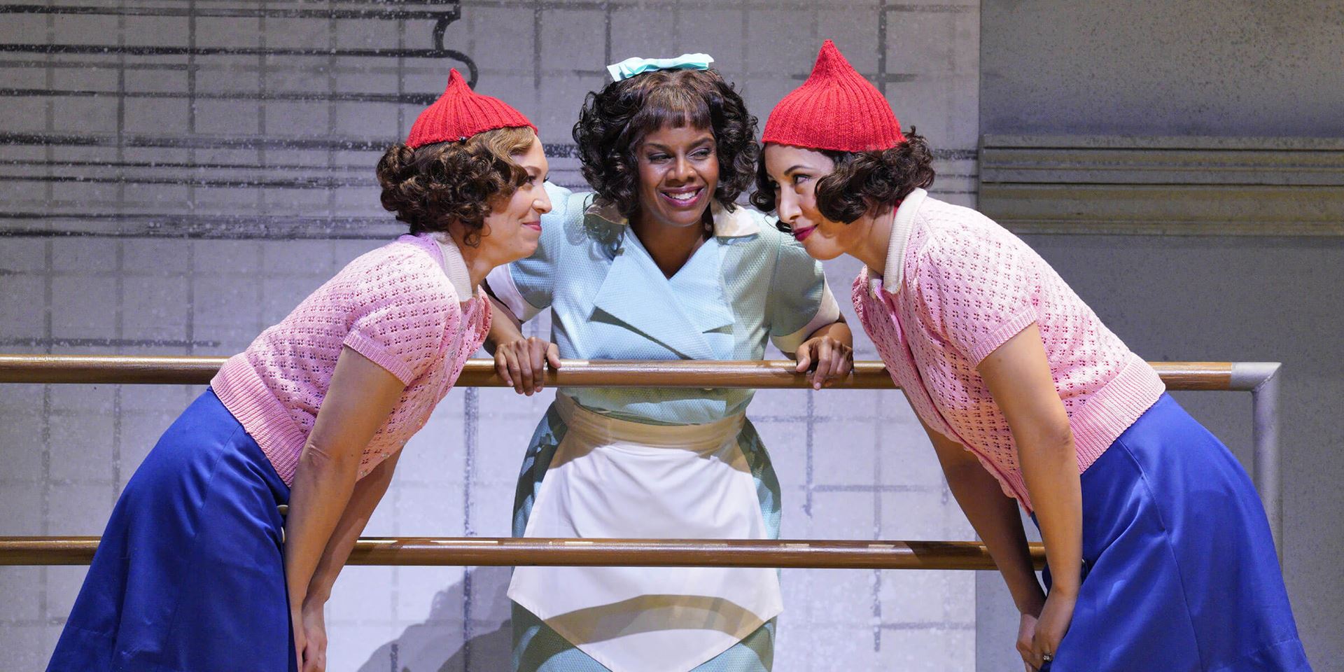 two women wearing similar costumes singing in front of a third women who stands between them