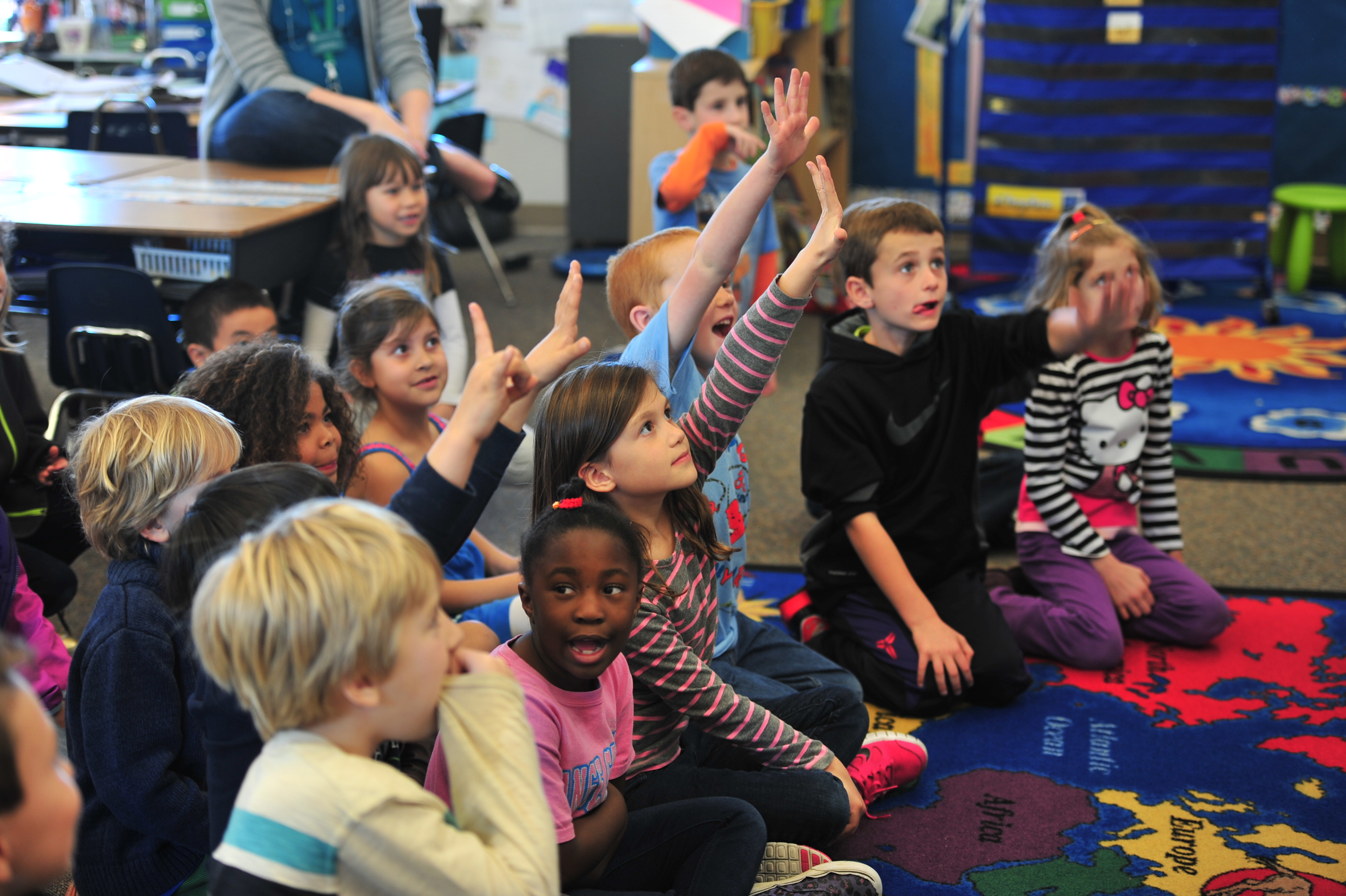 children sitting on floor in a classroom with their hands raised