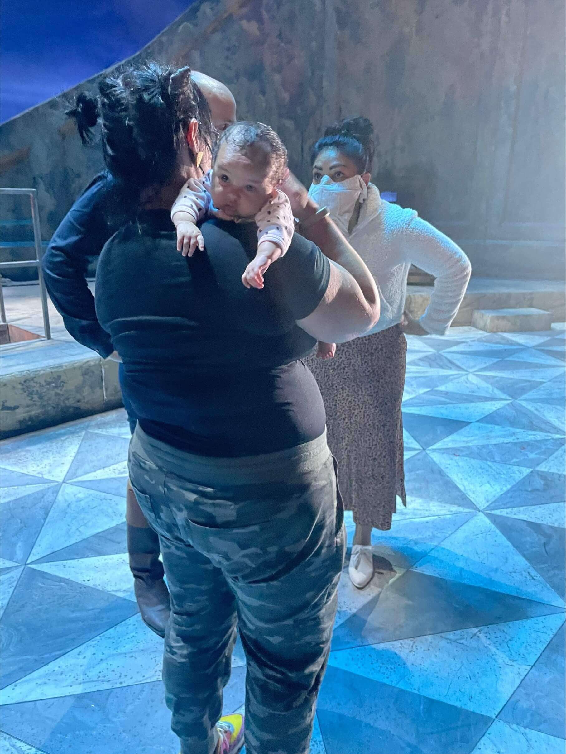 Three people with masks on talking and one is holding a baby