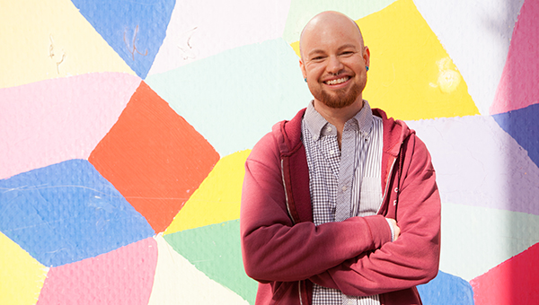 person standing in front of a colorful wall with their arms crossed and smiling